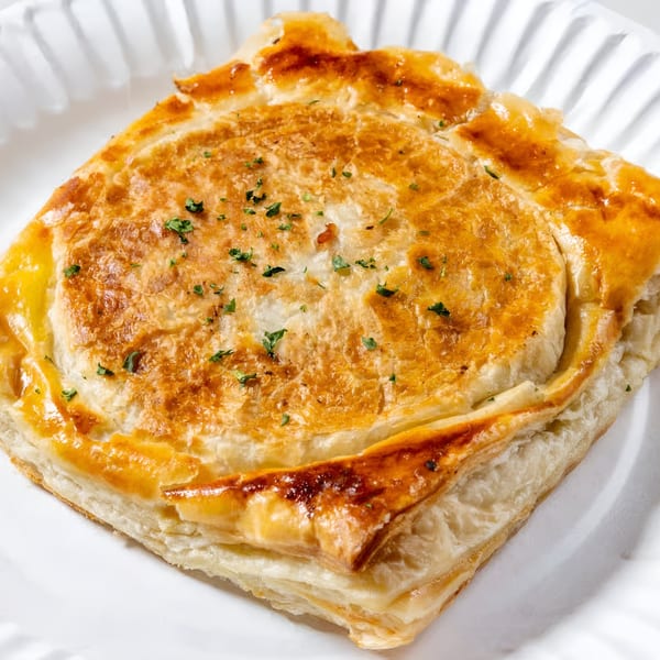 Golden-brown Greek pastry, possibly spanakopita or tiropita, on a white plate, garnished with herbs.