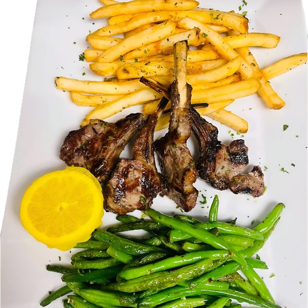 Four grilled lamb chops with a side of french fries, green beans, and a lemon wedge.