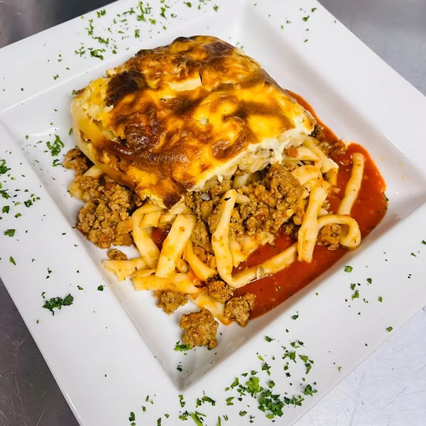 A Greek pastitsio with baked cheese topping, ground meat, and pasta in red sauce.