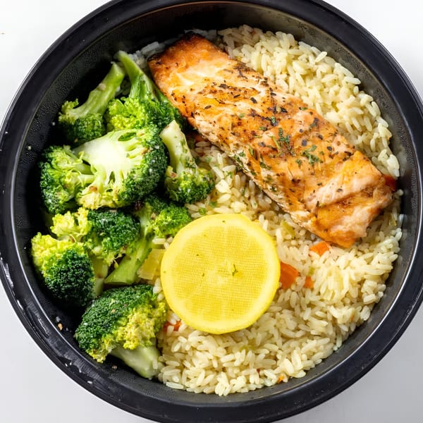 Greek Town's salmon with rice, broccoli, and a lemon slice in a black bowl.