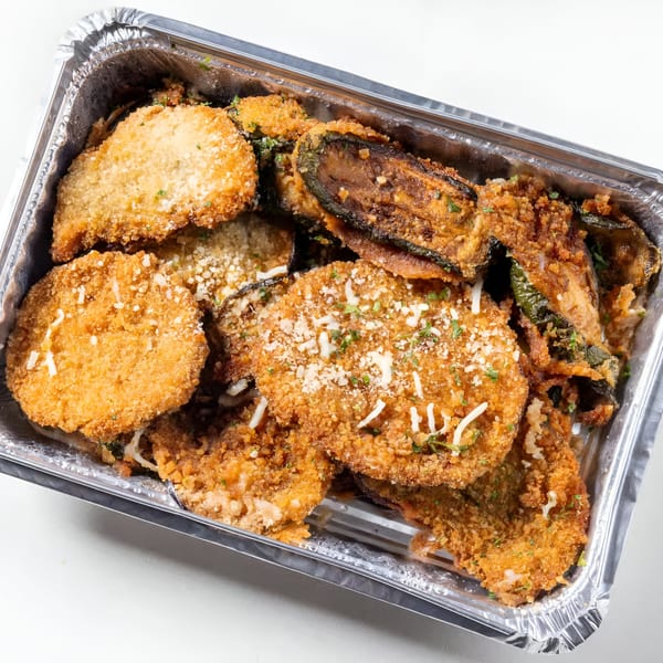 Crispy fried eggplant and zucchini slices, topped with cheese and herbs, in a foil takeout container.