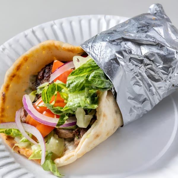 Greek gyro with meat, lettuce, tomatoes, and red onions, partially wrapped in foil on a white plate.